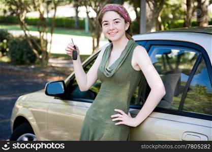 Pretty teen girl leaning on her new car and holding car keys.