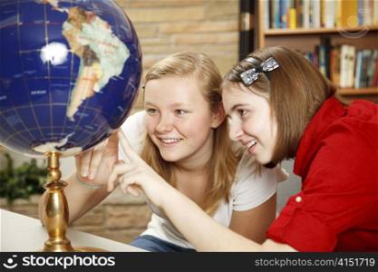 Pretty teen girls in the library looking up countries on the globe.