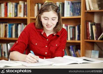 Pretty teenage girl doing her homework in the school library.