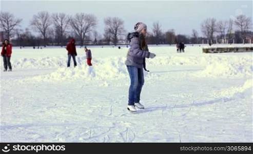pretty teenage girl goes skating in spiral position with back turn to camera by winter frozen lake