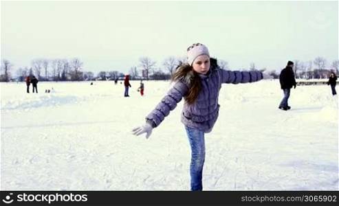 pretty teenage girl quickly goes skating in classic spiral position to camera by winter frozen lake