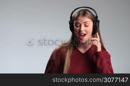 Pretty teenage girl touching headphones on her head with happy smile on white. Excited young brunette woman in big earphones dancing, swaying along with music and relaxing.