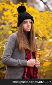 Pretty teenage girl wearing woolen hat with autumnal colours in the background looking into the distance