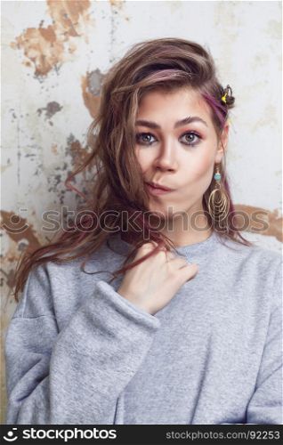 Pretty urban girl in grey sweatshirt making funny faces, grunge wall on background