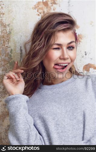 Pretty urban girl in grey sweatshirt making funny faces, grunge wall on background, close-up