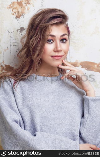 Pretty urban girl in grey sweatshirt smiling, grunge wall on background