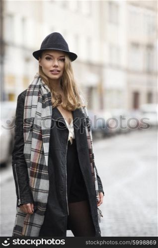pretty urban woman . with hat and scarf , she is walking on the street , looking in camera and smiling . freckles on the face