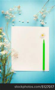 Pretty white flowers on blank paper with pen for greeting, Note , list or drawing on blue background, top view