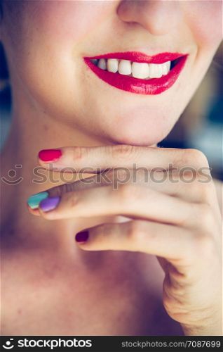 Pretty white woman with red sensual lipstick and white teeth colorful nail polish is looking into the mirror.