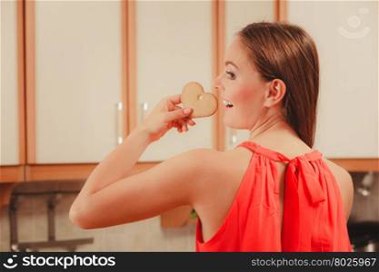 Pretty woman eating biting gingerbread cookie.. Pretty woman biting heart shape gingerbread cookie. Gorgeous girl relaxing while eating delicious biscuit food at home. Rear back view.