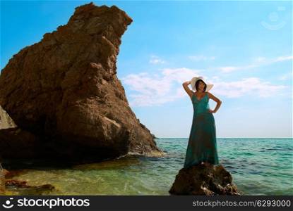 Pretty woman in dress and hat on the sea rock