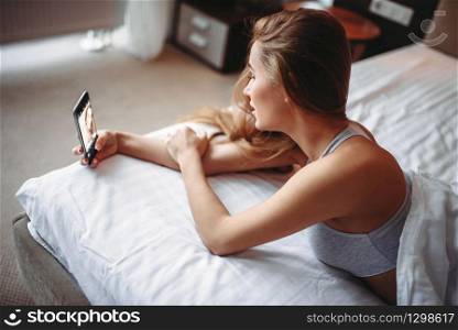 Pretty woman in underwear sitting in bed and makes selfie on phone. Good morning in bedroom. Pretty woman sitting in bed and makes selfie