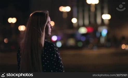 Pretty woman is standing alone on the night city street and waiting for man. Man gently hugging girl with one arm over night city background.Ukraine