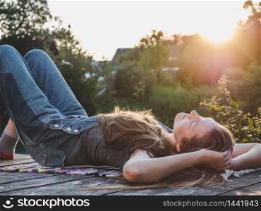 Pretty woman lying on a wooden terrace at sunset background. Closeup, side view, outdoor. Concept of rest and relaxation. Pretty woman lying on a wooden terrace