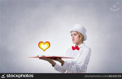 Pretty woman opening romantic book. Young woman in white cylinder and red bowtie with book in hands