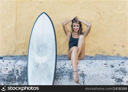 pretty woman sitting with surfboard leaning wall
