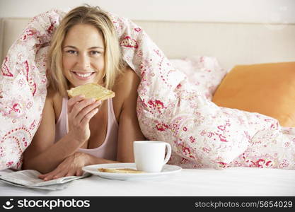 Pretty Woman Snuggled Under Duvet Eating Breakfast And Reading Newspaper