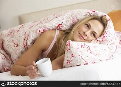 Pretty Woman Snuggled Under Duvet With Hot Drink