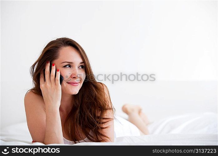 Pretty woman speaking on phone and lying on bed at home over white