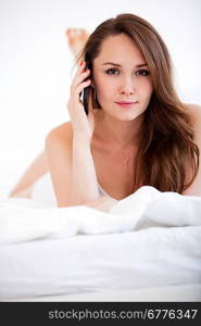 Pretty woman speaking on phone and lying on bed at home over white