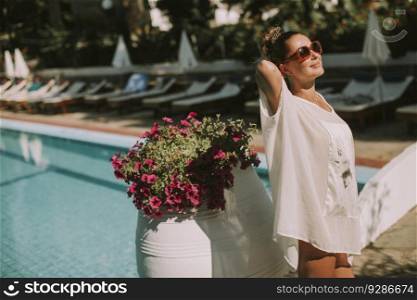 Pretty woman standing next to the swimming pool and enjoying the sun