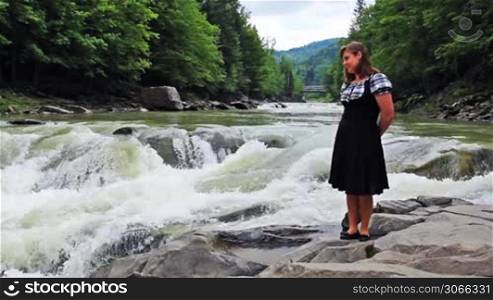 pretty woman stands in front of small waterfall at mountains Carpathians