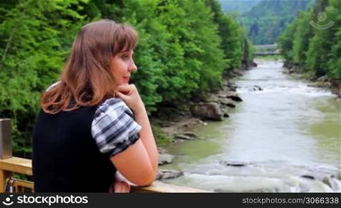 pretty woman stands near railing bridge and looks on waterfall in Carpathian Mountains, closeup