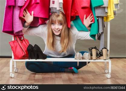 Pretty woman under clothes.. Pretty woman sitting on the floor under clothing from wardrobe. Young happy undecided shopper girl bought new clothes. Shopaholic concept.