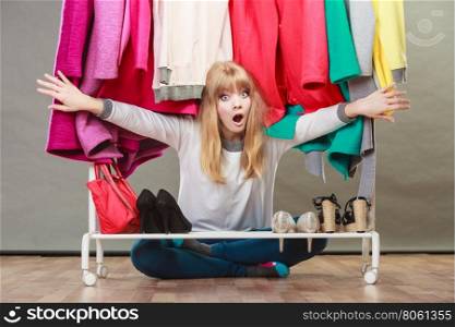 Pretty woman under clothes.. Suprised pretty woman sitting under clothing from wardrobe. Young undecided shopper girl bought new clothes. Shopaholic concept.