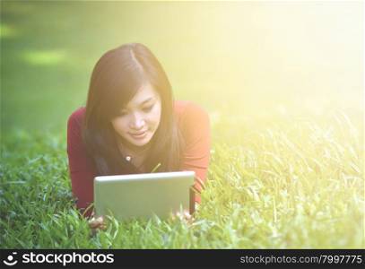 pretty woman using tablet outdoor laying on grass with flare light