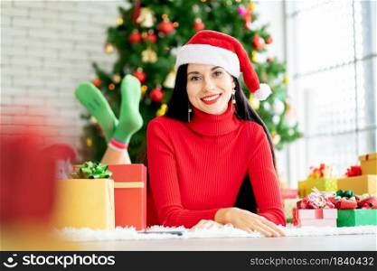 Pretty woman with Christmas costume lie on floor and look at camera with smiling stay at home with the present and Christmas tree as background.