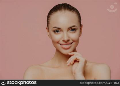 Pretty woman with glowing skin, chin touch, cares for complexion, nude, cosmetology, pink background. Beauty.