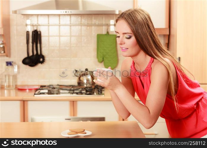 Pretty woman with heart shape gingerbread cookies drinking tea or coffee at home. Gorgeous young girl with hot beverage relaxing in kitchen.. Woman with gingerbread cookies drinking tea coffee