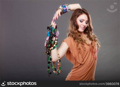 Pretty woman with jewelry necklaces ring bracelets. Pretty young woman wearing bracelets and rings holding many plentiful of precious jewelry necklaces beads. Portrait of gorgeous fashion girl in studio on gray.
