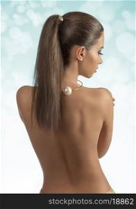 pretty woman with long brown hair-style ponytail showing her sexy naked back and wearing golden accessories