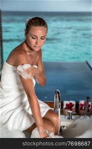 Pretty woman with pleasure taking bath with foam in the bathroom with great view on the sea, spending summer vacation on the luxury spa resort on Maldives