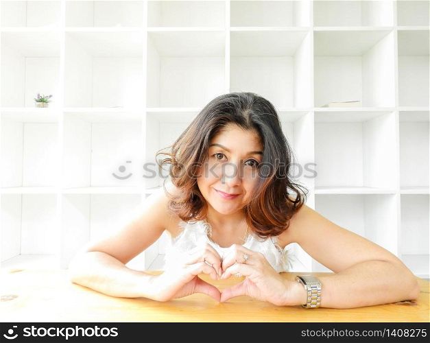 Pretty woman with smiley happy face making heart shape by her hands.