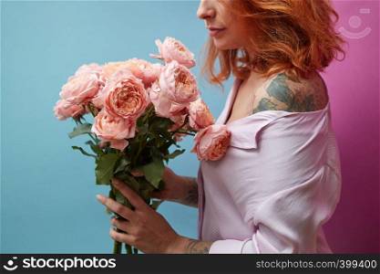 Pretty woman with tattoo holding bouquet of pink bouquet around a double blue pink background with copy space. St. Valentine's Day. Gentle pink roses in the hands of a girl with a tattoo on a double pink blue background with copy space for text. Birthday present