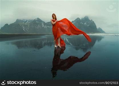 Pretty woman with waving cape on Reynisfjara beach scenic photography. Picture of person with hills on background. High quality wallpaper. Photo concept for ads, travel blog, magazine, article. Pretty woman with waving cape on Reynisfjara beach scenic photography