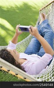 Pretty young adult Caucasian brunette female lying in hammock using PDA.