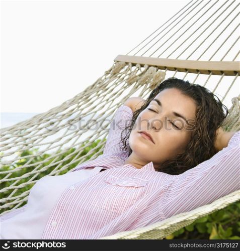 Pretty young adult Caucasian brunette female lying in hammock with arms behind head sleeping.