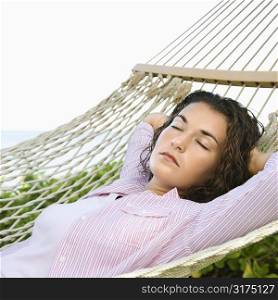 Pretty young adult Caucasian brunette female lying in hammock with arms behind head sleeping.