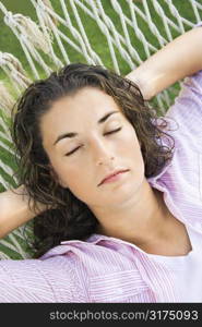Pretty young adult Caucasian brunette female lying in hammock with hands behind head sleeping.