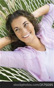 Pretty young adult Caucasian brunette female lying in hammock with hands behind head smiling.