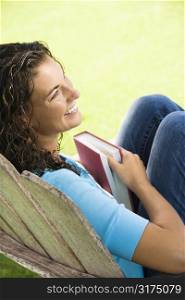 Pretty young adult Caucasian brunette female sitting in chair holding book and smiling.