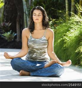 Pretty young adult Caucasian brunette woman sitting in lotus position practicing yoga.