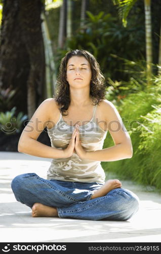 Pretty young adult Caucasian brunette woman sitting in lotus position practicing yoga with hands at heart center.