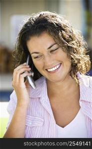Pretty young adult Caucasian brunette woman talking on cell phone and smiling.