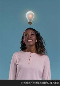 Pretty young african lady standing and thinking with light bulb overhead. Idea concept