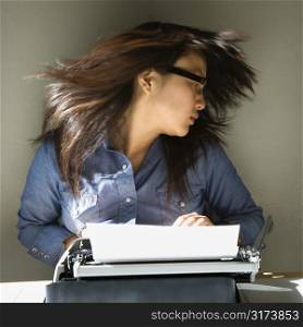 Pretty young Asian woman sitting at typewriter swinging head and hair around.